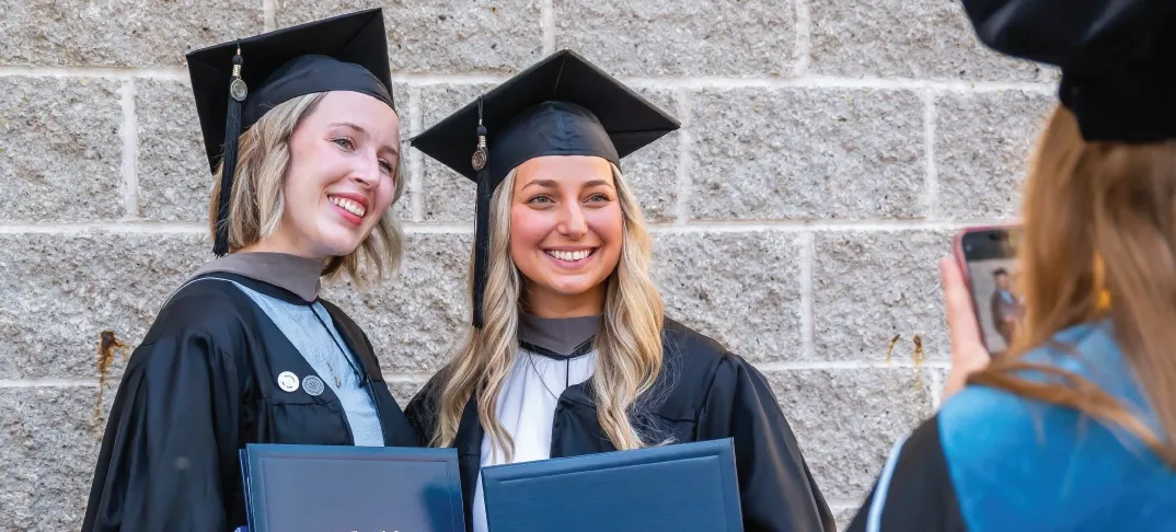 Two master degree graduates smiling and posing together outdoors.